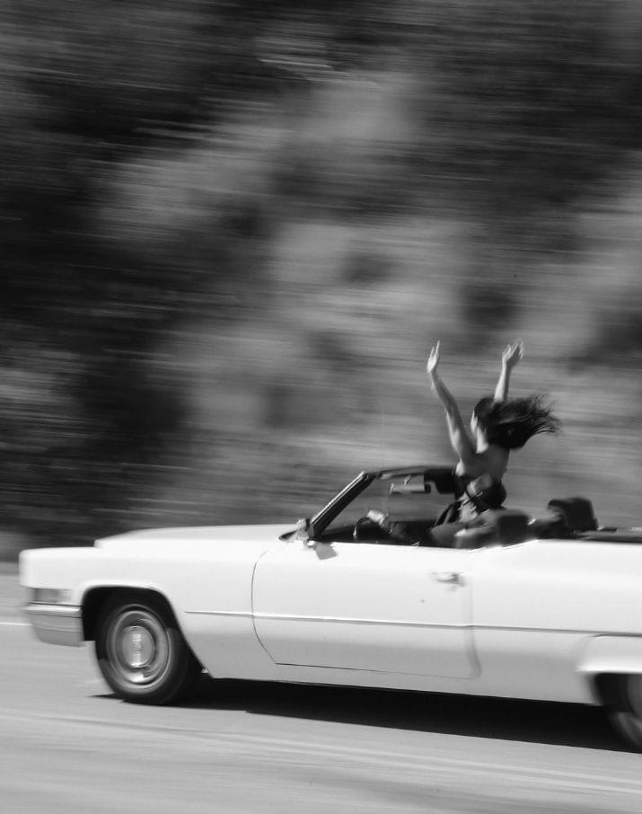 Mujer con los brazos levantados disfrutando de libertad en un coche descapotable en movimiento